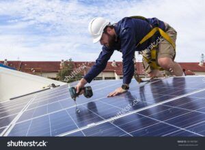 photo solar panel technician with drill installing solar panels on roof